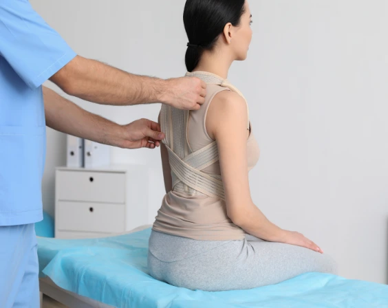 Doctor fitting back brace on patient in clinic.
